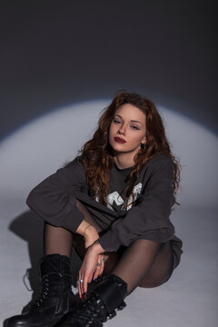 Fashion girl in stylish clothes with a sweatshirt, tights and boots sits on the floor in the studio