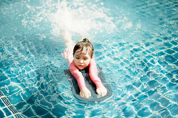 A little asian girl in swimming in the pool. Cute girl playing in outdoor swimming pool on a hot...