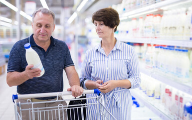 Mature family of retirees considering bottle of milk in dairy section of supermarket