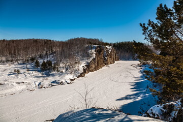 Winter landscape with a large stone, forest, sky, frozen river from a high bank