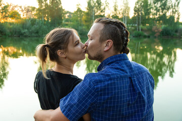 Beautiful, happy couple have fun on the background of nature. A handsome guy in a shirt gently hugs a smiling girl with blond hair. Lifestyle and travel concept.