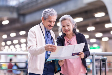 Asian active senior retirement couple is looking at the map for direction inside airport terminal for second honeymoon pensioner travel and urban metro train transportation concept