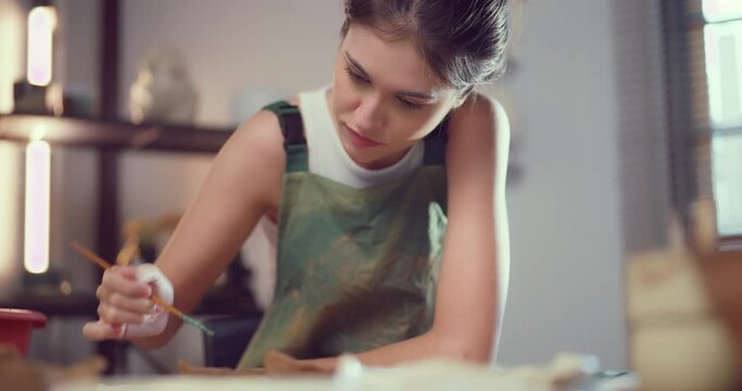 Concentrated female artist meticulously painting a decorative pattern on a ceramic plate in her studio.