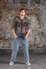 A modern young man with a stylish hairstyle stands near a wall on a dark background