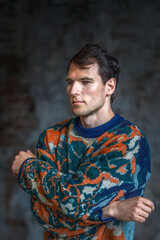 A modern young man with a stylish hairstyle stands against a brick wall on a dark background.