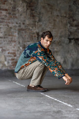 A modern young man with a stylish hairstyle stands against a brick wall on a dark background