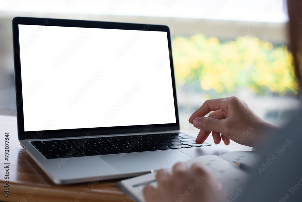 Wall mural Mockup blank screen laptop computer. Business woman using and typing on laptop with blank white screen on wooden table in modern loft cafe, web template design for online marketing