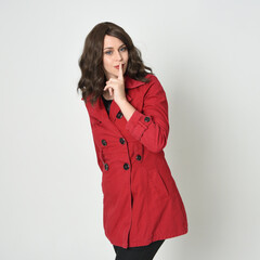 close up portrait of beautiful brunette woman model, wearing red trench coat jacket.
isolated on white studio. finger half to mouth in secretive shushing gesture.