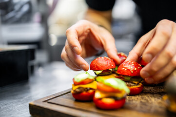  skilled chef meticulously assembles a vibrant mini burgers on a wooden board, showcasing culinary...