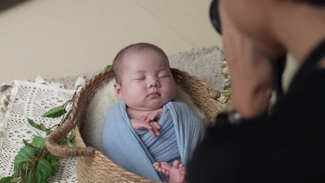 A Japanese photographer in his 30s taking a newborn photo of a 32-day-on Taiwanese baby wrapped in a blue wrap 30代の日本人カメラマンが青いおくるみを巻かれた生後32日の台湾人の赤ちゃんのニューボーンフォトを撮影する様子