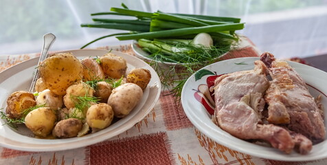 Plates with green onions, potatoes and smoked chicken close-up on the background of the kitchen tablecloth