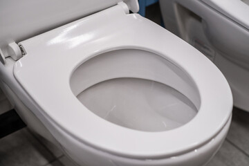 A close up of an empty toilet seat, a plumbing fixture in a bathroom. The ceramic rectangle bowl, circular seat, and plumbing beneath are visible