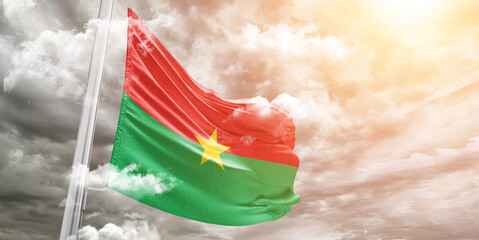 Burkina Faso national flag cloth fabric waving on beautiful cloudy Background.