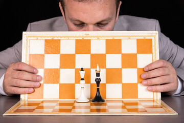 A man, a businessman sits at a chessboard. On the board are a black king and a white queen....