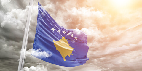 Kosovo national flag cloth fabric waving on beautiful cloudy Background.