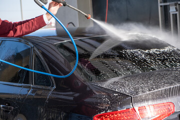 A man washes off the foam while washing the car. A vehicle is engulfed in soapy foam during a car...