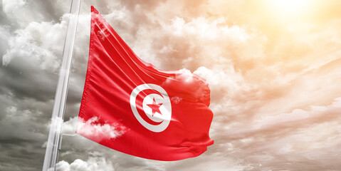 Tunisia national flag cloth fabric waving on beautiful cloudy Background.