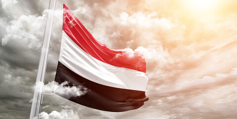 Yemen national flag cloth fabric waving on beautiful cloudy Background.