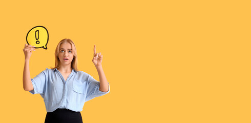 Young businesswoman holding speech bubble with exclamation mark and pointing at something on yellow...