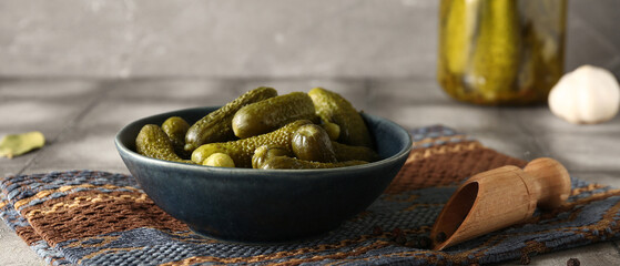Bowl and jar of tasty pickled cucumbers with different spices on grey tile table
