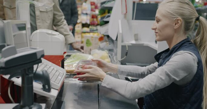 Cheerful young woman cashier scanning products working at checkout terminal in supermarket. Retail business and groceries store concept.