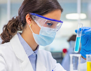 Close-up of a focused female scientist examining a test tube in a laboratory, adhering to safety protocols - 772097136