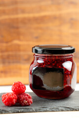jar of raspberry jam with berries on a wooden background
