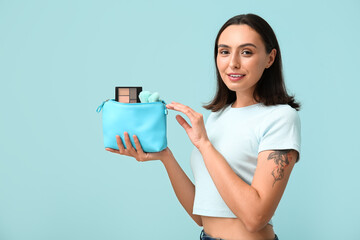 Beautiful young woman with cosmetic bag full of makeup products on blue background