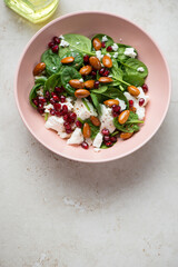 Salad with spinach, feta, pomegranate seeds and almonds served in a roseate bowl, vertical shot on a light-beige stone background, copy space, high angle view