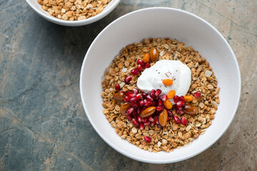 Granola bowl with yogurt, pomegranate seeds and nuts, horizontal shot on a grey and beige granite background, high angle view
