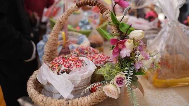 a basket with traditional pastries, Easter Kulich cake and colored eggs, in front of other baskets with Easter food. Many baskets are displayed on the table for the consecration and blessing of Easter