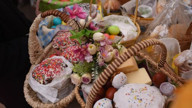 a basket with traditional pastries, Easter Kulich cake and colored eggs, in front of other baskets with Easter food. Many baskets are displayed on the table for the consecration and blessing of Easter