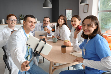 Team of doctors taking selfie on coffee break at table in hospital kitchen