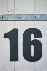 Nummer 16 Hausnummer Sechzehn. Schwarze Ziffern auf einer weisen Holztür