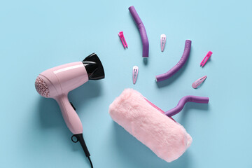 Hair dryer with cosmetic bag, curlers and hairpins on blue background - obrazy, fototapety, plakaty