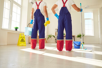 Legs of a team of professional janitors in uniform going to wash the floor with detergent at home...