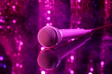 Modern microphone on glass table against blurred lights, closeup