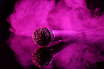 Modern microphone with smoke on glass table against dark background