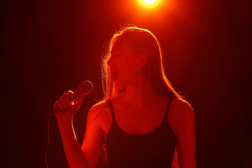 Young woman with modern microphone singing on dark background