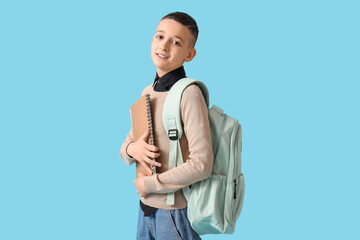 Fototapeta premium Smiling young schoolboy with backpack and notebook ready for education and learning on blue background