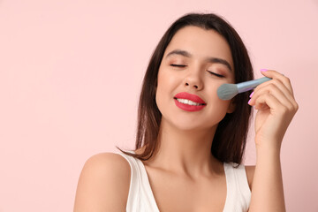 Beautiful young happy woman with stylish makeup and brush on pink background