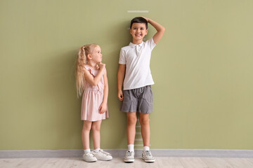 Cute little kids measuring height near green wall