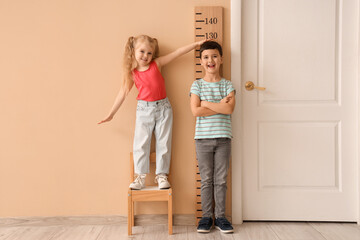 Cute little kids measuring height near wooden stadiometer