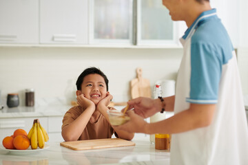 Happy kid looking at father making breakfast