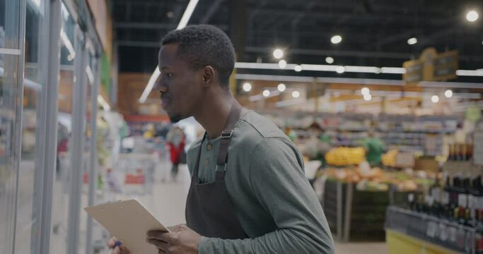 African American guy supermarket worker doing inventory writing information checking food. Retail business and consumption concept.