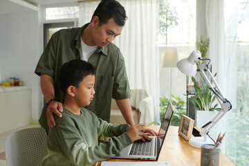 Father helping preteen son working on laptop