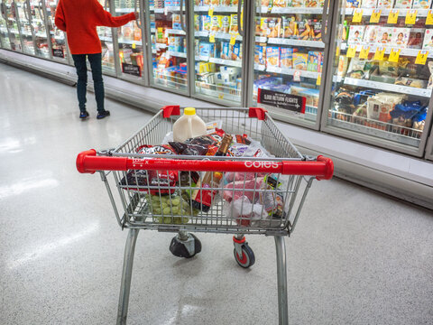 A shopping trolley with a variety of grocery items at front of freezer in Coles supermarket. A routine shopping scenario in Australia. Coles is a well-known Australian supermarket chain
