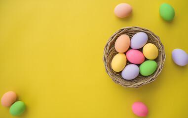 Top view of multi-colored Easter eggs in basket on yellow background with copy space happy easter