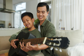 Smiling father teaching son to play chords