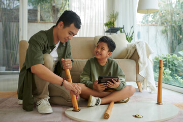 Smiling Vietnamese father and son assembling coffee table in living room